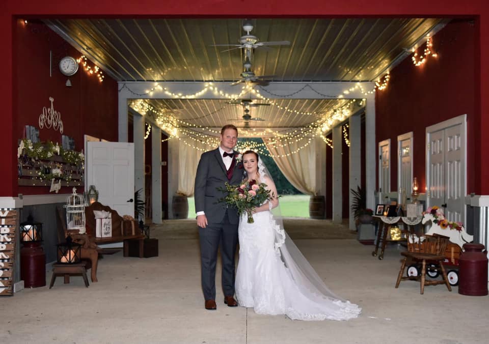 bride and groom standing in front of red barn at Big Wedd Barn